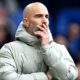 Enzo Maresca, looks on during the Premier League match between Chelsea and Brighton at Stamford Bridge. He is wearing a grey coat and holding his face.