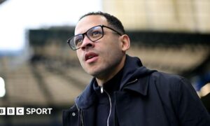 Close-up of Liam Rosenior. He has short black hair and is wearing black-rimmed glasses and a navy coat.