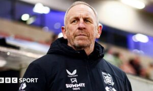 Hull FC head coach John Cartwright watches on from the sidelines in a club-issued black coat
