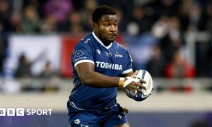 Nathan Jibulu running with the ball to his left side grasped in both hands during a match for Sale