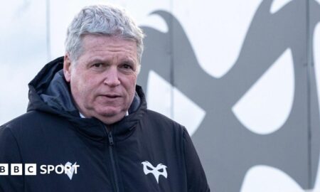 Lance Bradley wearing an Ospreys jacket in front of an Ospreys logo at Brewery Field
