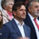 FAW chief executive Noel Mooney, in a blue suit and open neck white shirt, stands during a game.