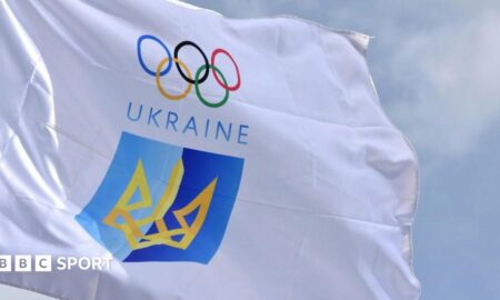 White flag of the National Olympic Committee of Ukraine, featuring the Olympic rings above the word Ukraine and a blue and yellow crest